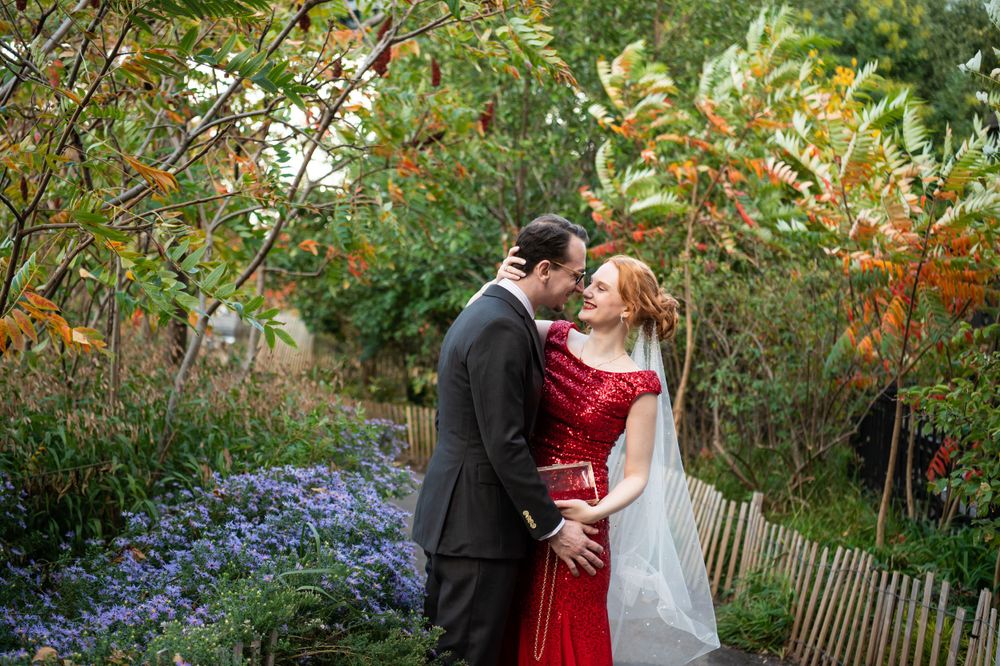 A romantic moment captured in a garden with purple flowers and autumn foliage, featuring a red dress and formal attire.