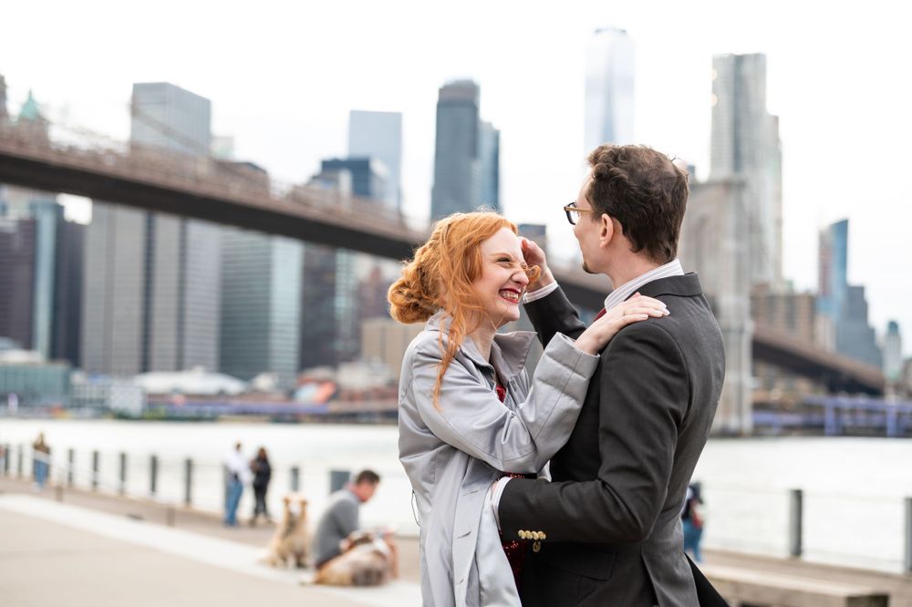 A couple shares a romantic moment near Brooklyn Bridge with the Manhattan skyline in the background.