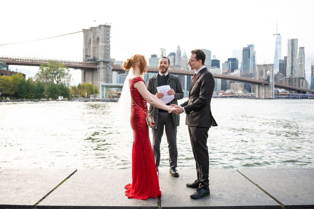 An intimate wedding ceremony takes place along the waterfront with the Brooklyn Bridge and Manhattan skyline in the background.
