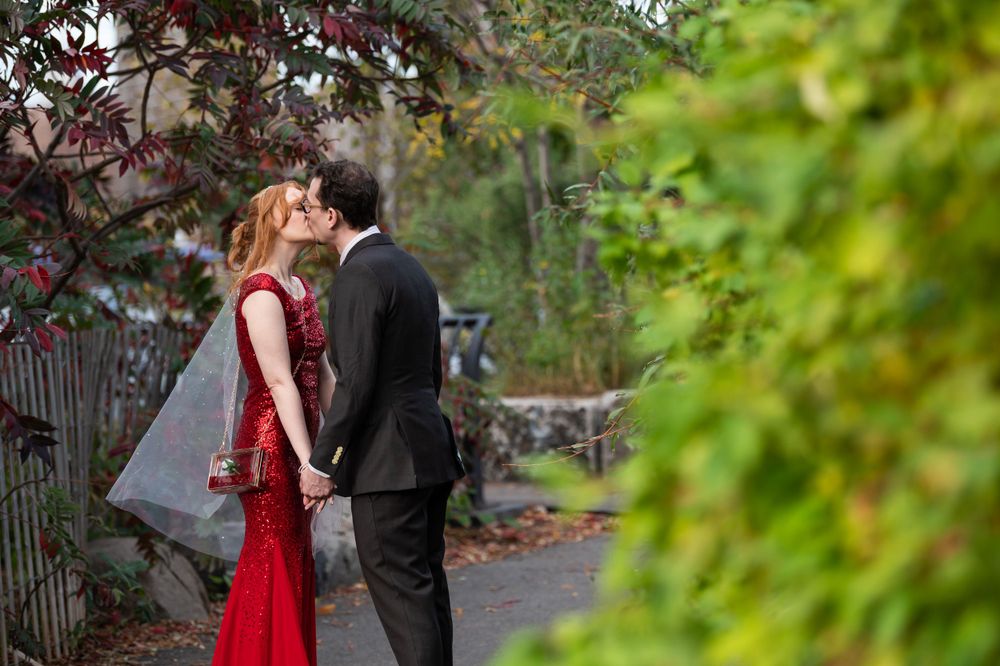 A couple sharing a romantic moment in a garden setting, with the woman wearing an elegant red dress.