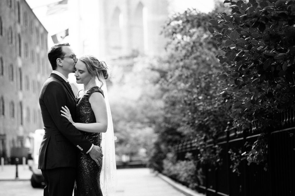 A romantic black and white wedding moment captured on a city street with greenery in the background.