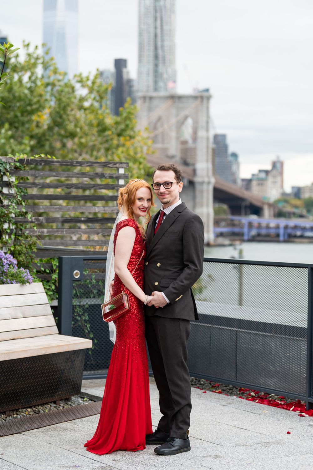 A couple poses together on a rooftop terrace in Brooklyn with the NYC skyline behind them.