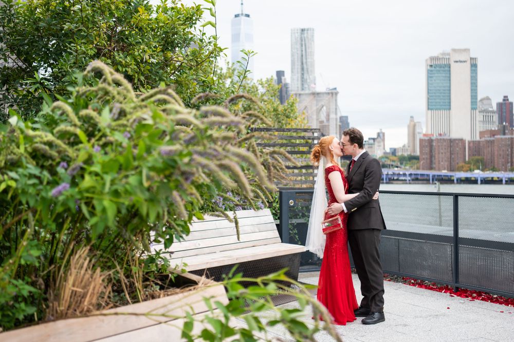 A couple shares a romantic moment on a rooftop terrace with lush greenery and city skyline in the background.