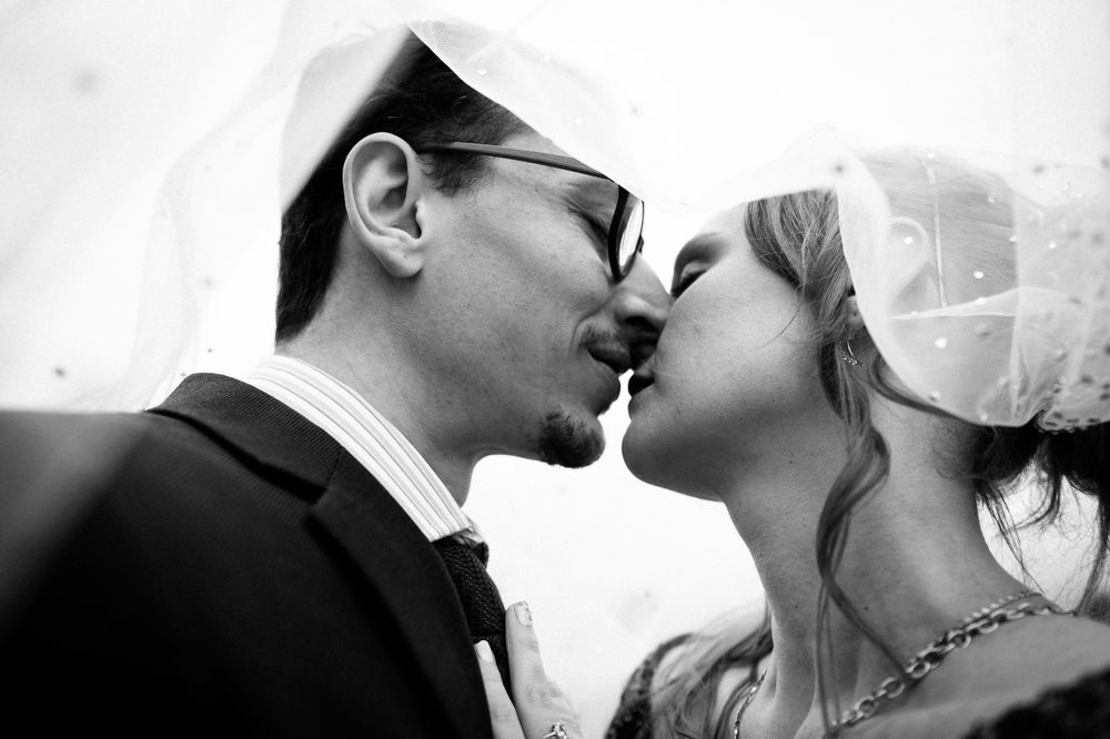 Black and white close-up photograph of a romantic wedding kiss between a couple with the bride wearing a veil.