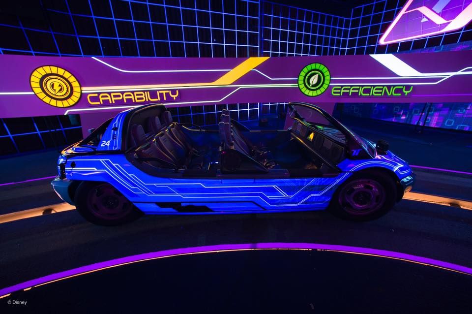 A futuristic blue racing vehicle on a virtual neon track with glowing grid lines and purple lighting effects.