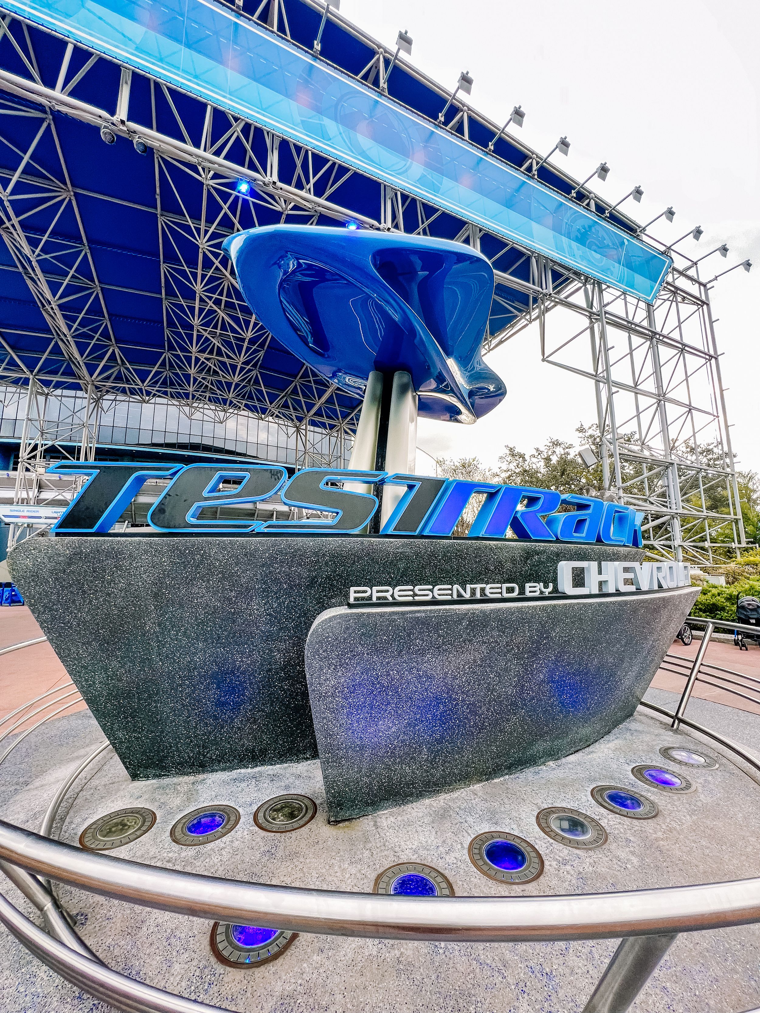 The Test Track attraction entrance at Epcot features a blue angular structure with metallic design elements and illuminated accents.