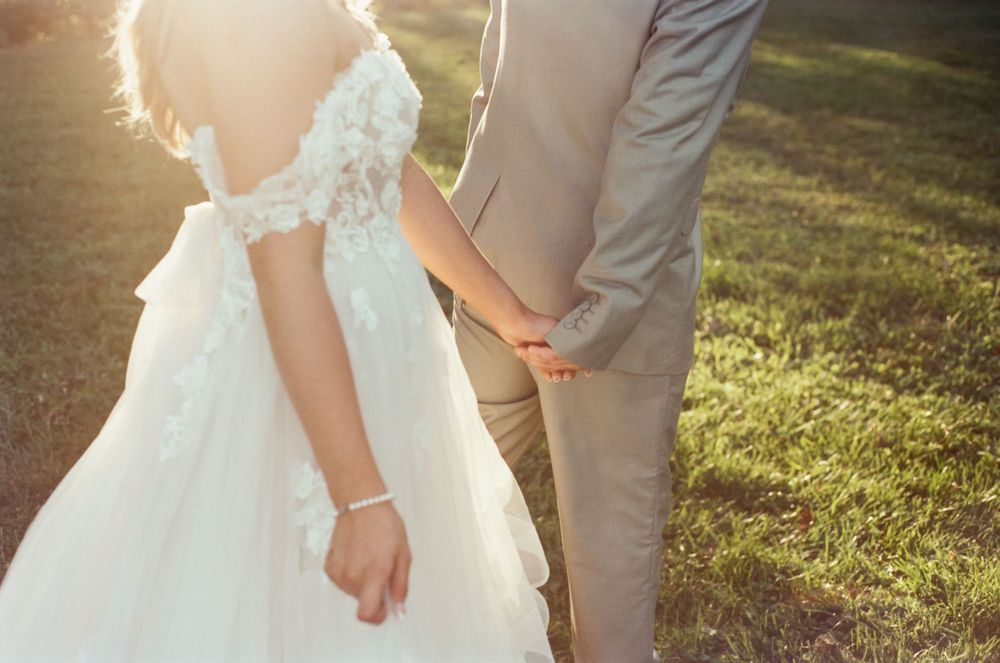 Close-up shot of bride and groom holding hands in sunlit outdoor setting.