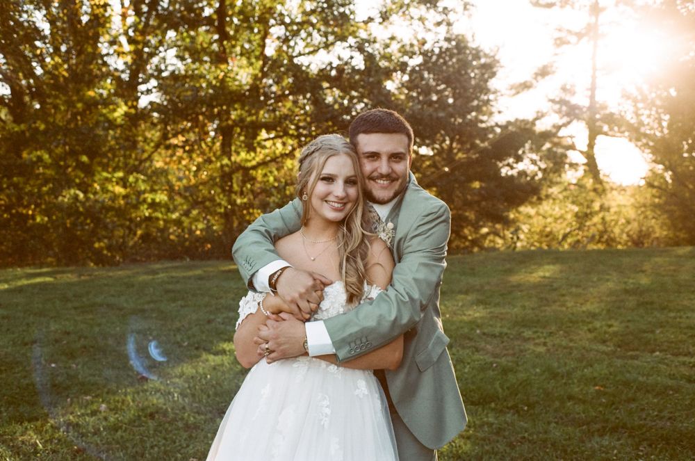 Romantic sunset wedding portrait showing couple embracing in white dress and sage green suit outdoors.