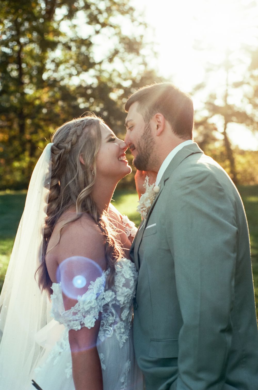 Wedding couple shares an intimate moment in the golden sunlight with trees in background.