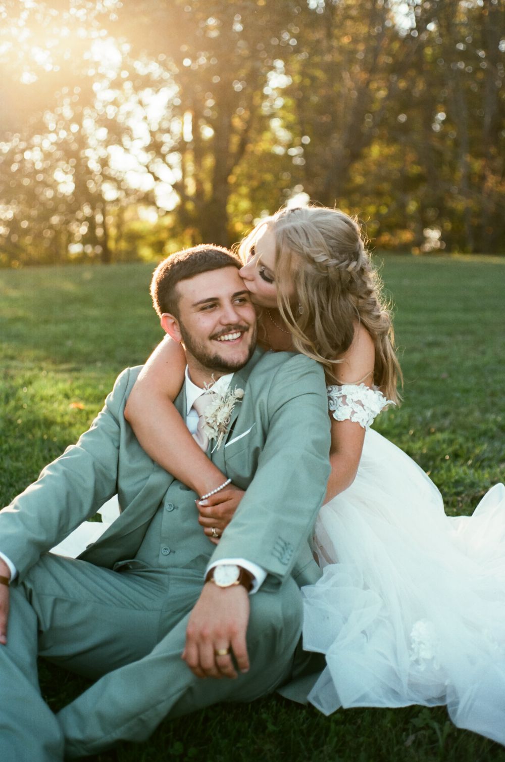 Joyful wedding couple laughing together on grass during sunset outdoor photo session.