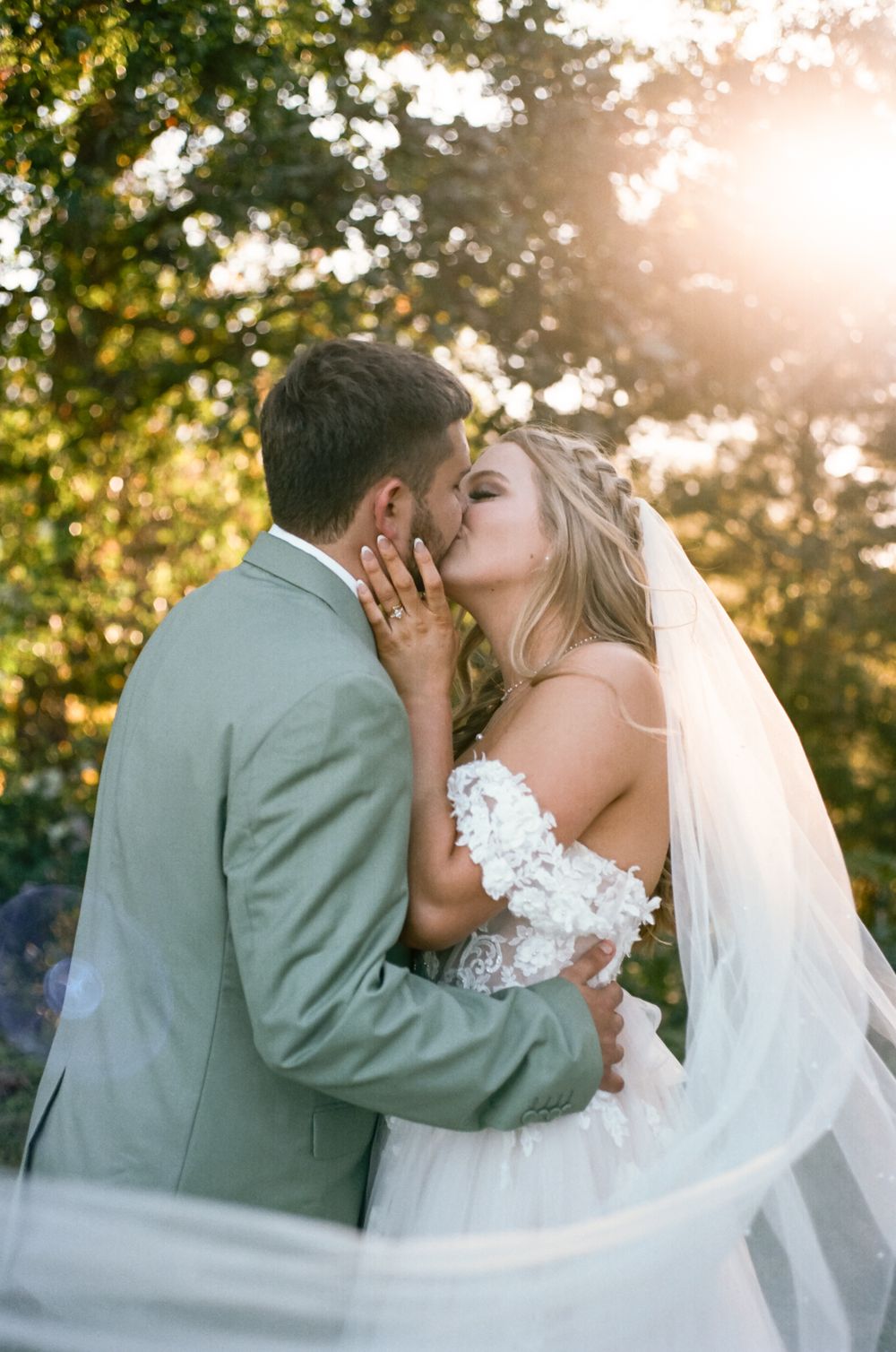 Romantic wedding portrait with couple sharing tender moment against sunset and trees.