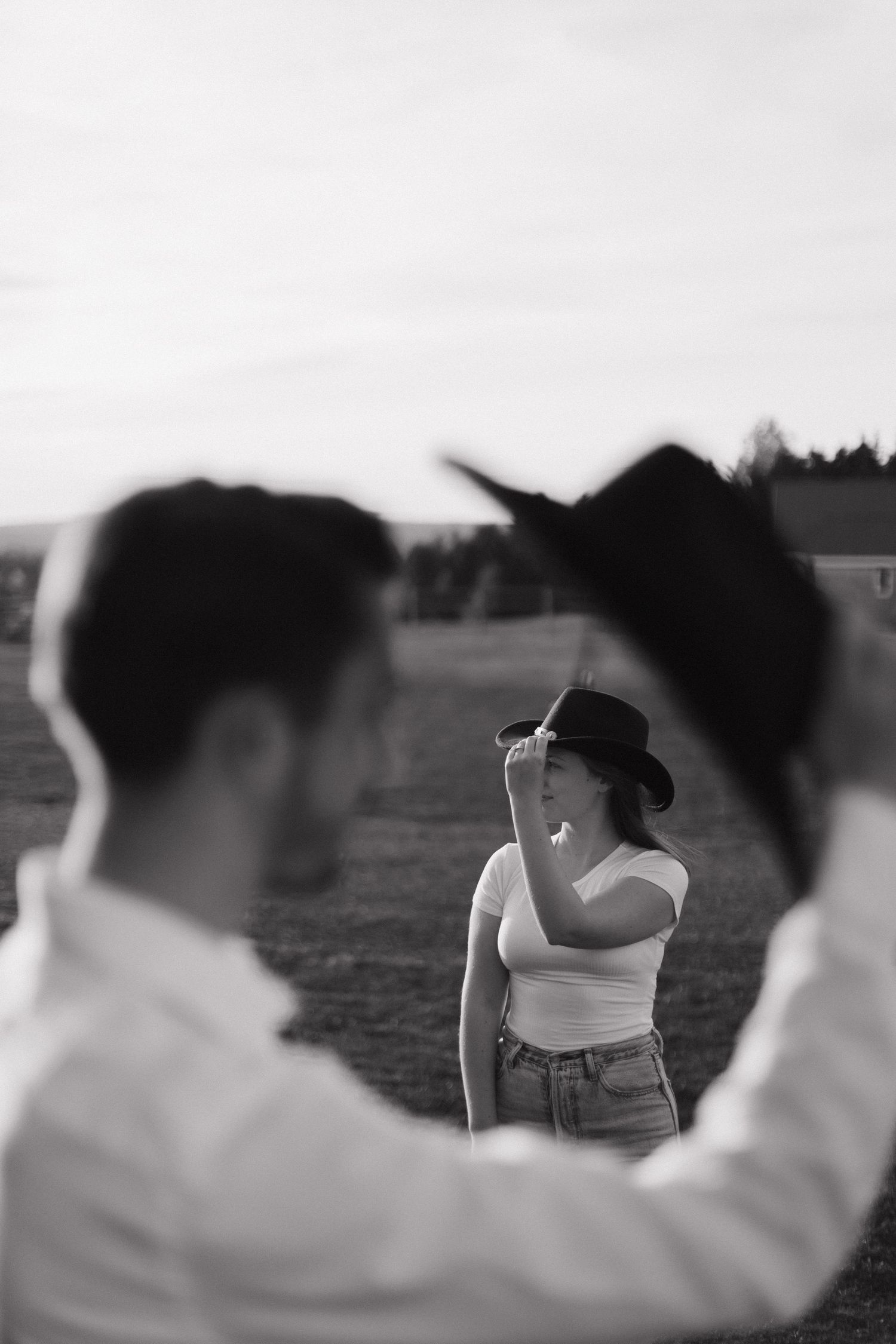 Black and white artistic photo shows someone in a cowboy hat and jeans viewed through a silhouetted frame in the foreground.