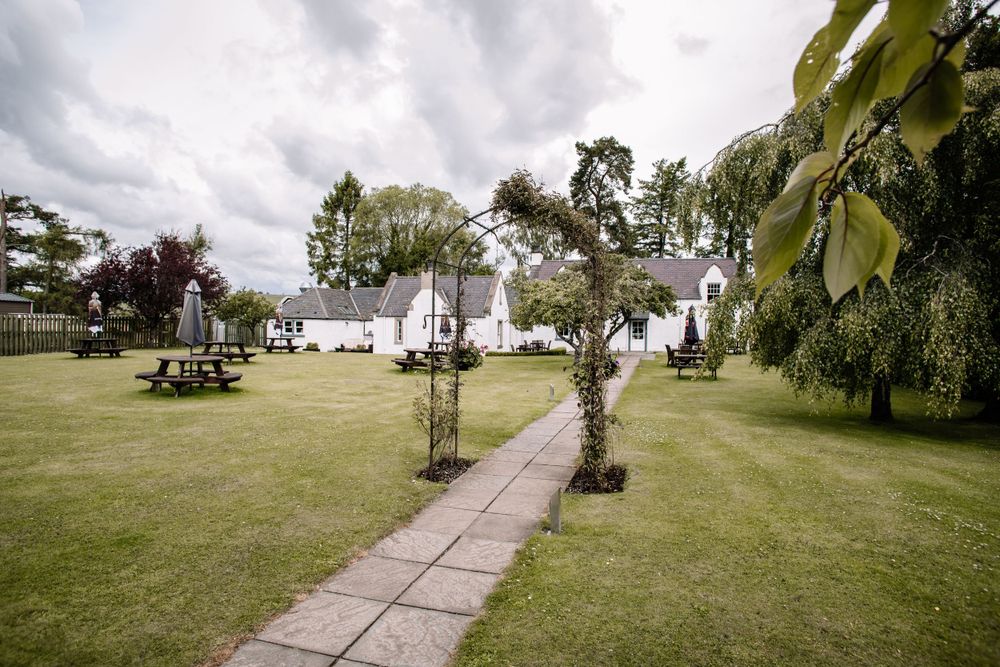 White buildings connected by a stone pathway in a lush garden setting under cloudy skies.
