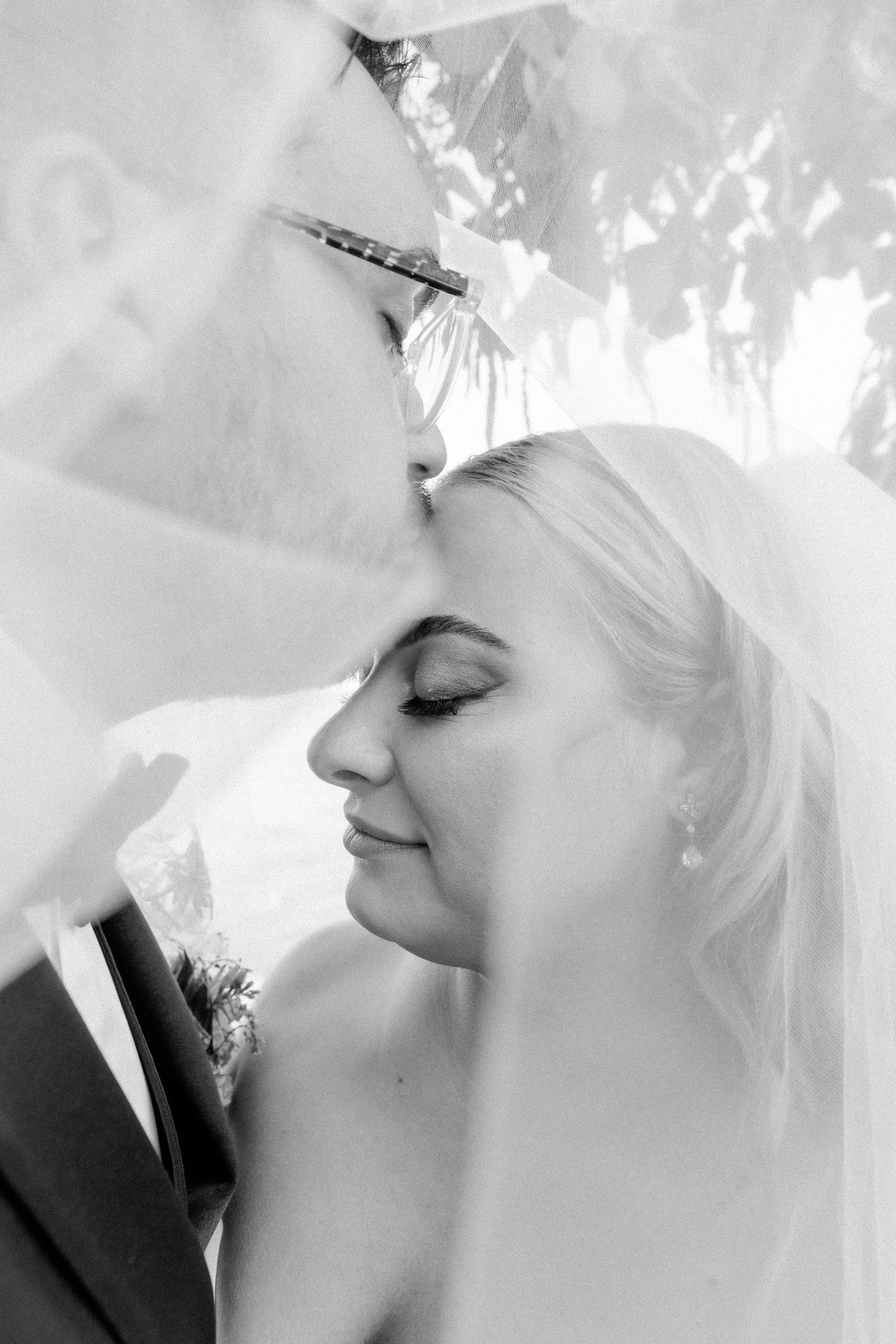 An intimate black and white portrait of a couple sharing a tender moment under a wedding veil.