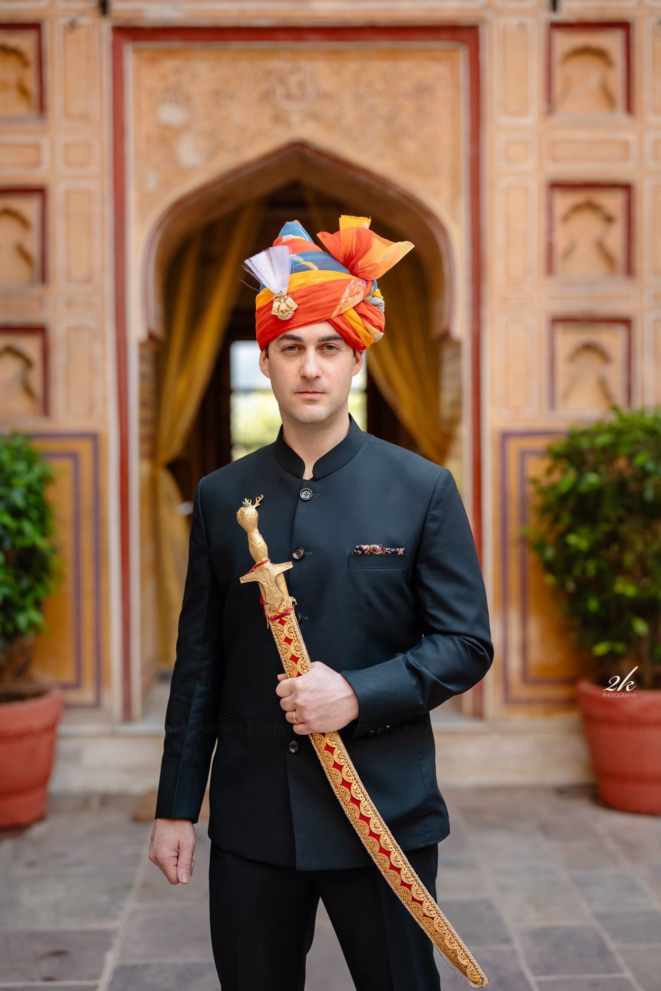 Traditional Indian formal attire with colorful turban and decorative sword at historic palace entrance.