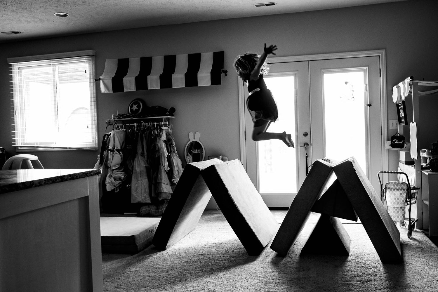 A dramatic black and white photograph shows someone leaping between two geometric structures in a home setting.