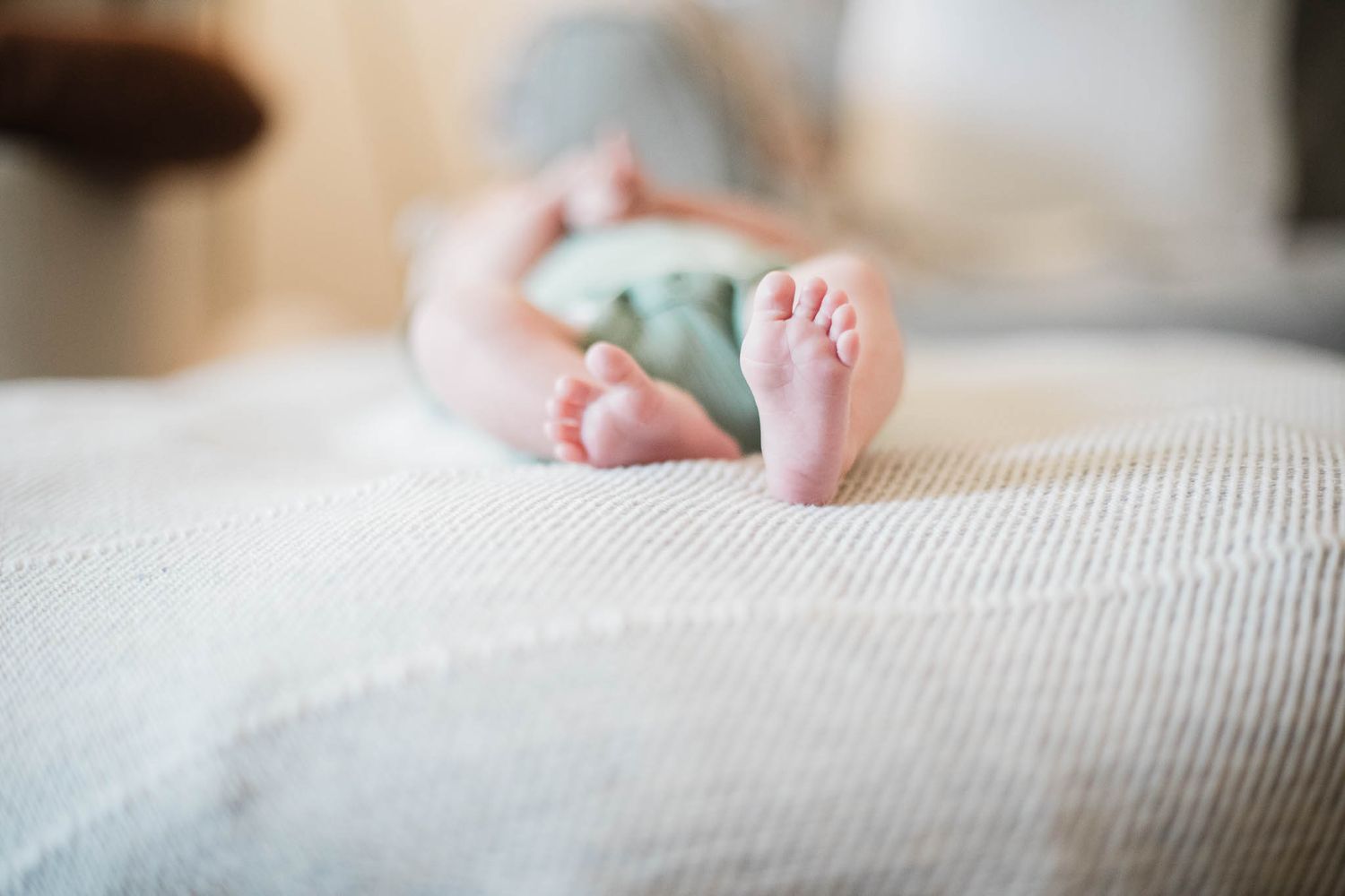 Close-up view of tiny baby feet resting on white textured bedding while holding a small blue object.