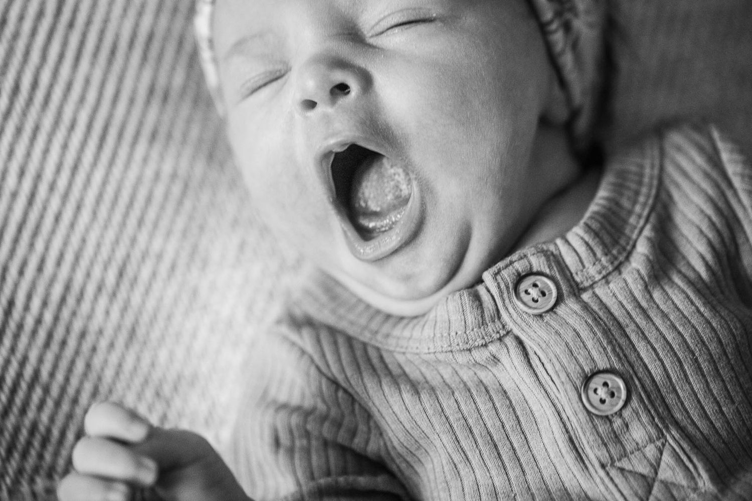 Black and white closeup of a yawning baby wearing a knit sweater with buttons.