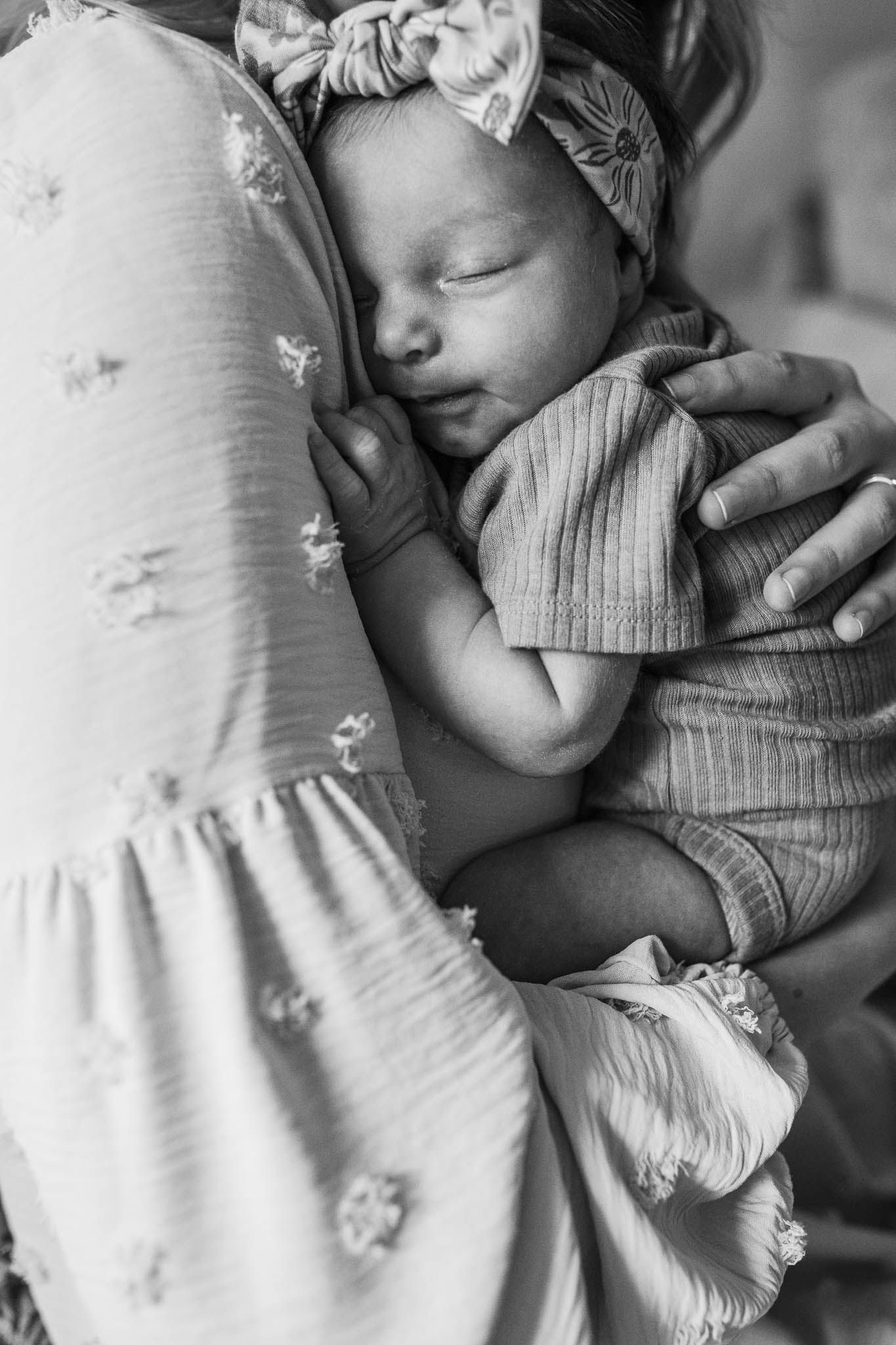 A tender black and white photo of a sleeping infant in a striped onesie being cradled in loving arms.