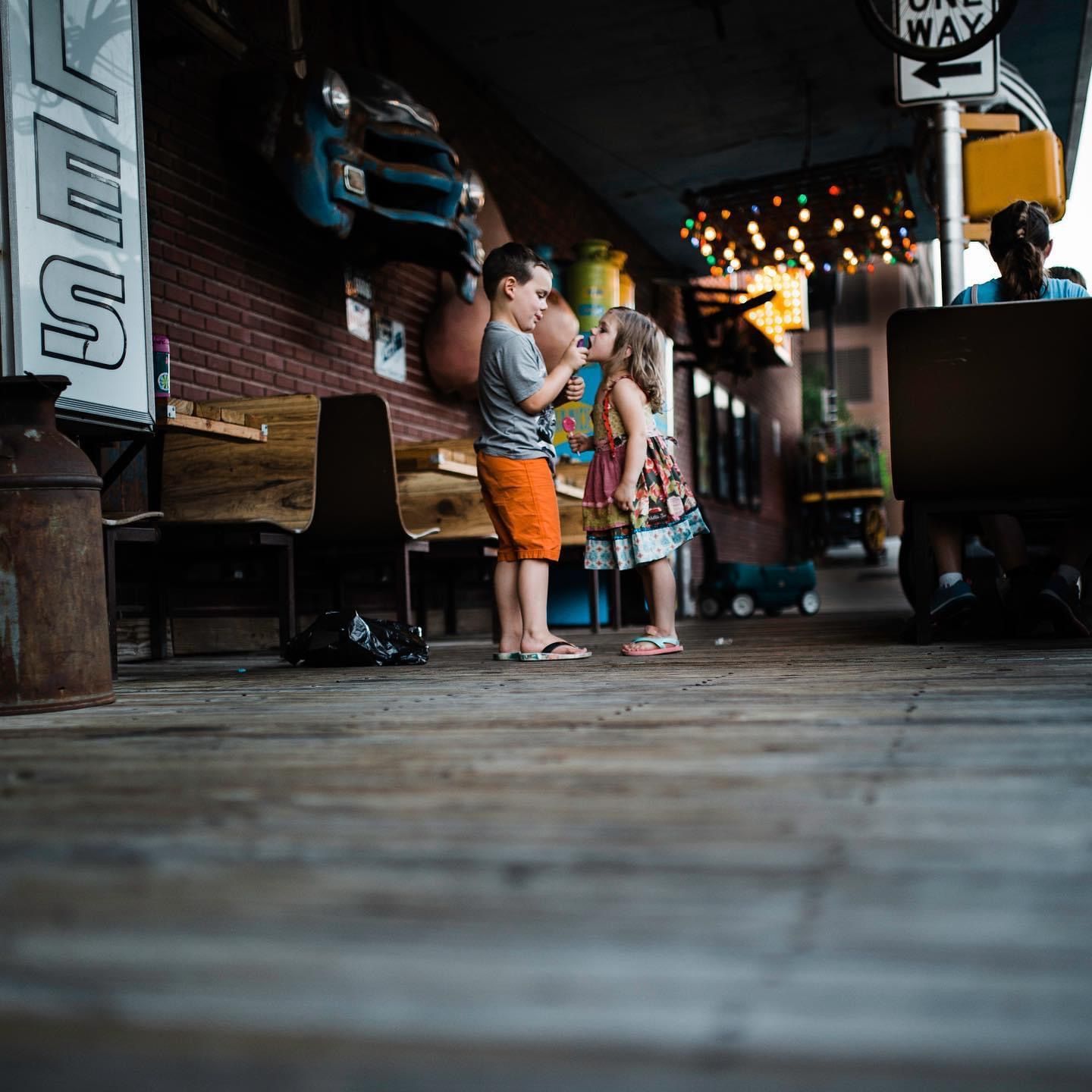 People waiting in line outside a brick building at dusk with warm lighting and a low perspective view.