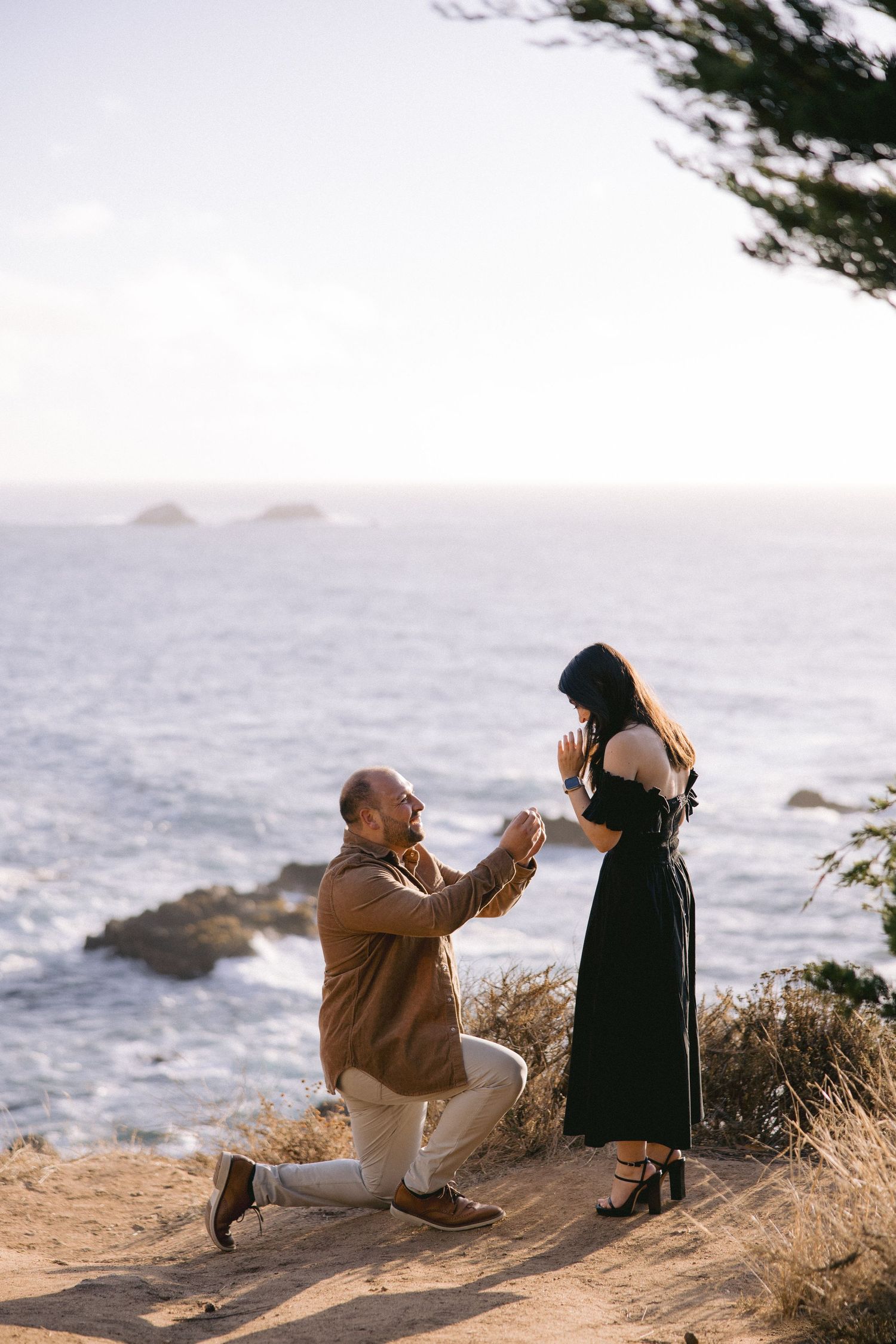 A romantic seaside marriage proposal takes place on a cliff overlooking the ocean at sunset.