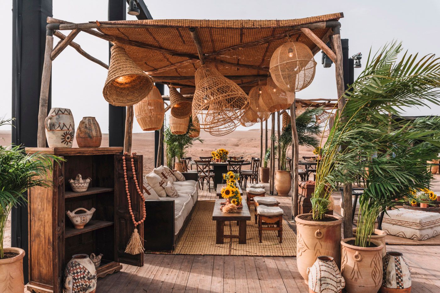 Bohemian outdoor patio space with wooden decor, hanging lanterns, potted plants and rustic furniture under a canopy shade.