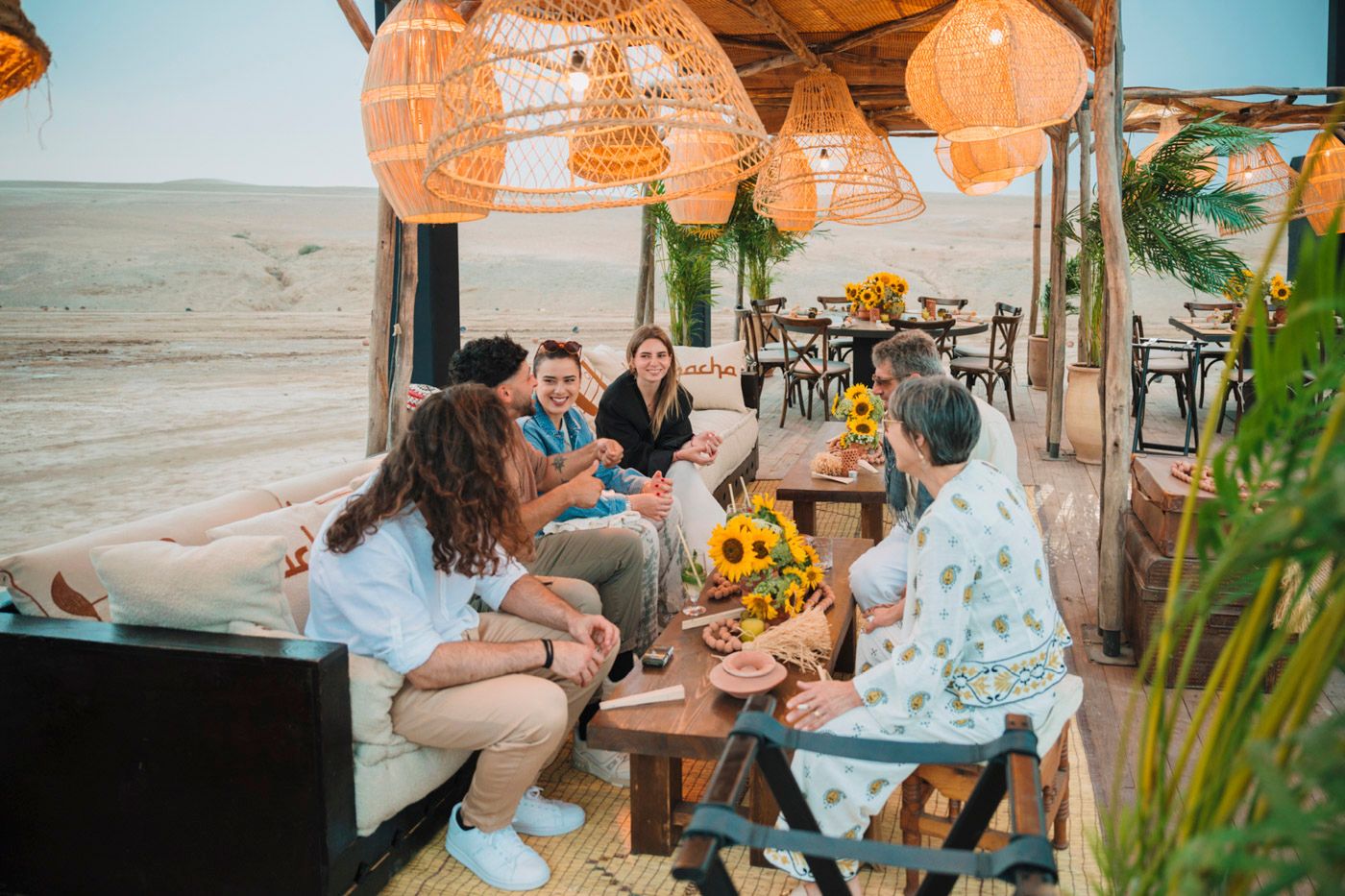 A festive beach party setup with orange paper lanterns and guests dining at decorated tables.