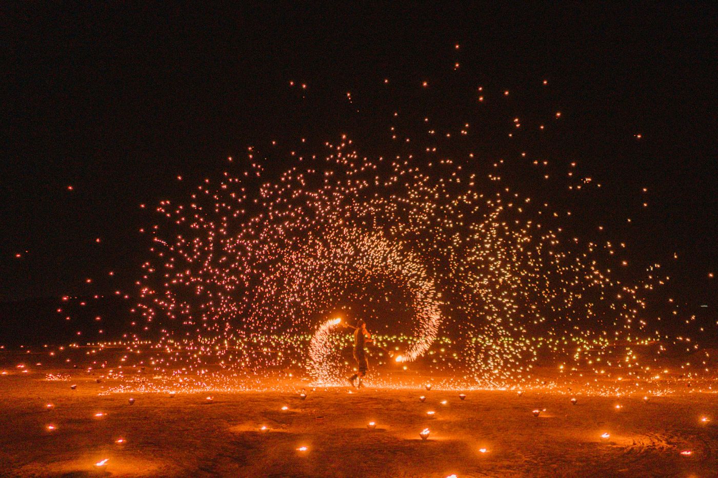 Glowing steel wool spinning creates a dramatic spiral of orange sparks against a dark night sky.