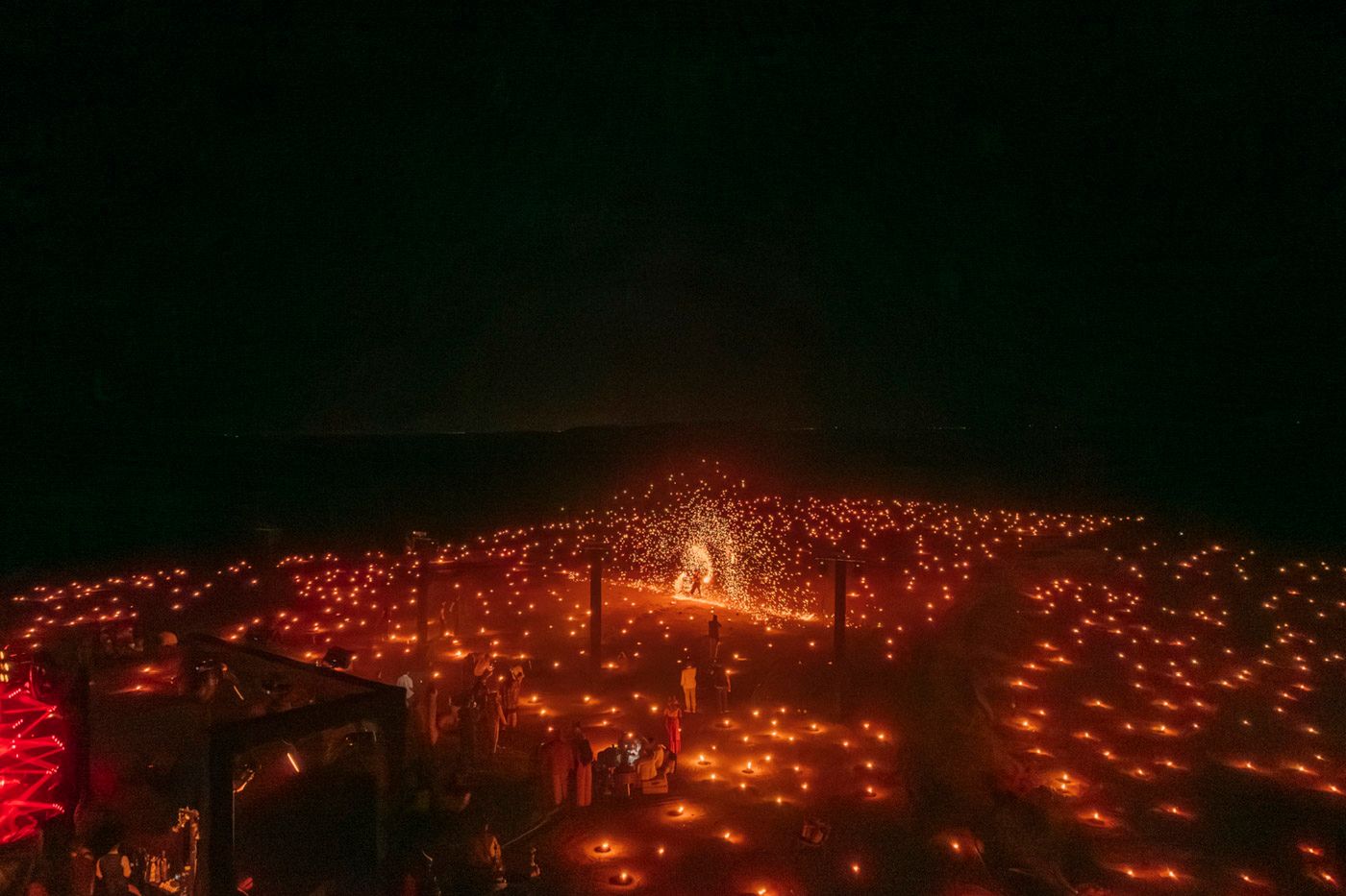 Aerial view of a dark concert venue illuminated by thousands of glowing red lights surrounding a central brightly lit stage.