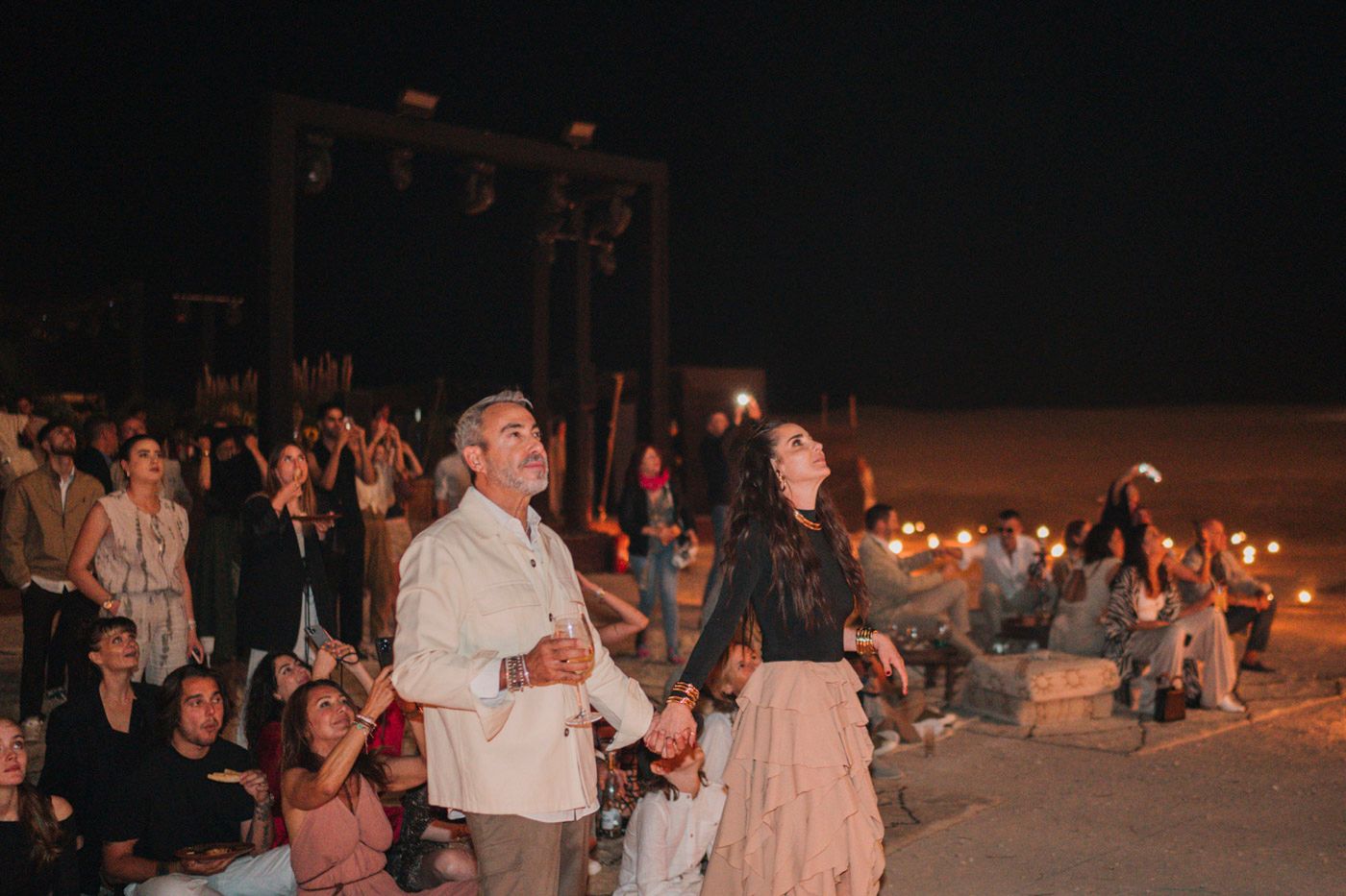 People enjoying a romantic nighttime beach celebration with candles and string lights creating an atmospheric ambiance.