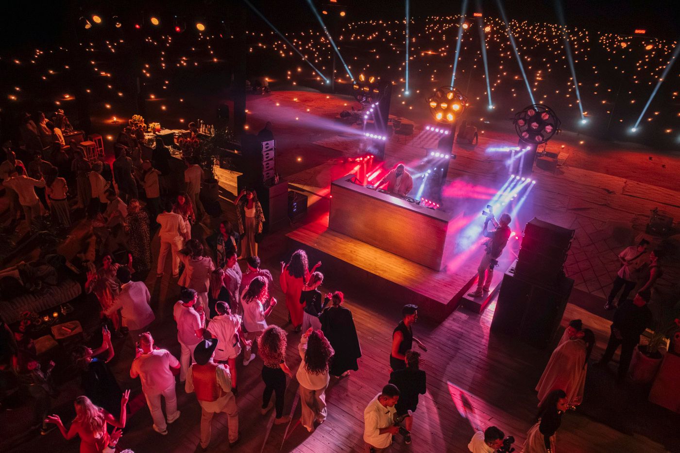 Aerial view of a crowded nightclub dance floor with vibrant pink and purple lighting effects illuminating the space.