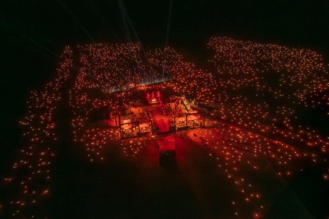 Stunning aerial view of a red-lit venue surrounded by thousands of glowing lights creating a magical atmosphere.