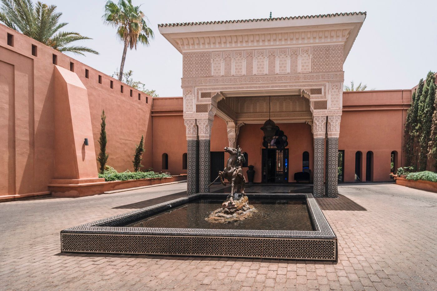 Traditional Moroccan fountain and archway architecture in coral-colored courtyard with palm trees at luxury hotel in Marrakech.