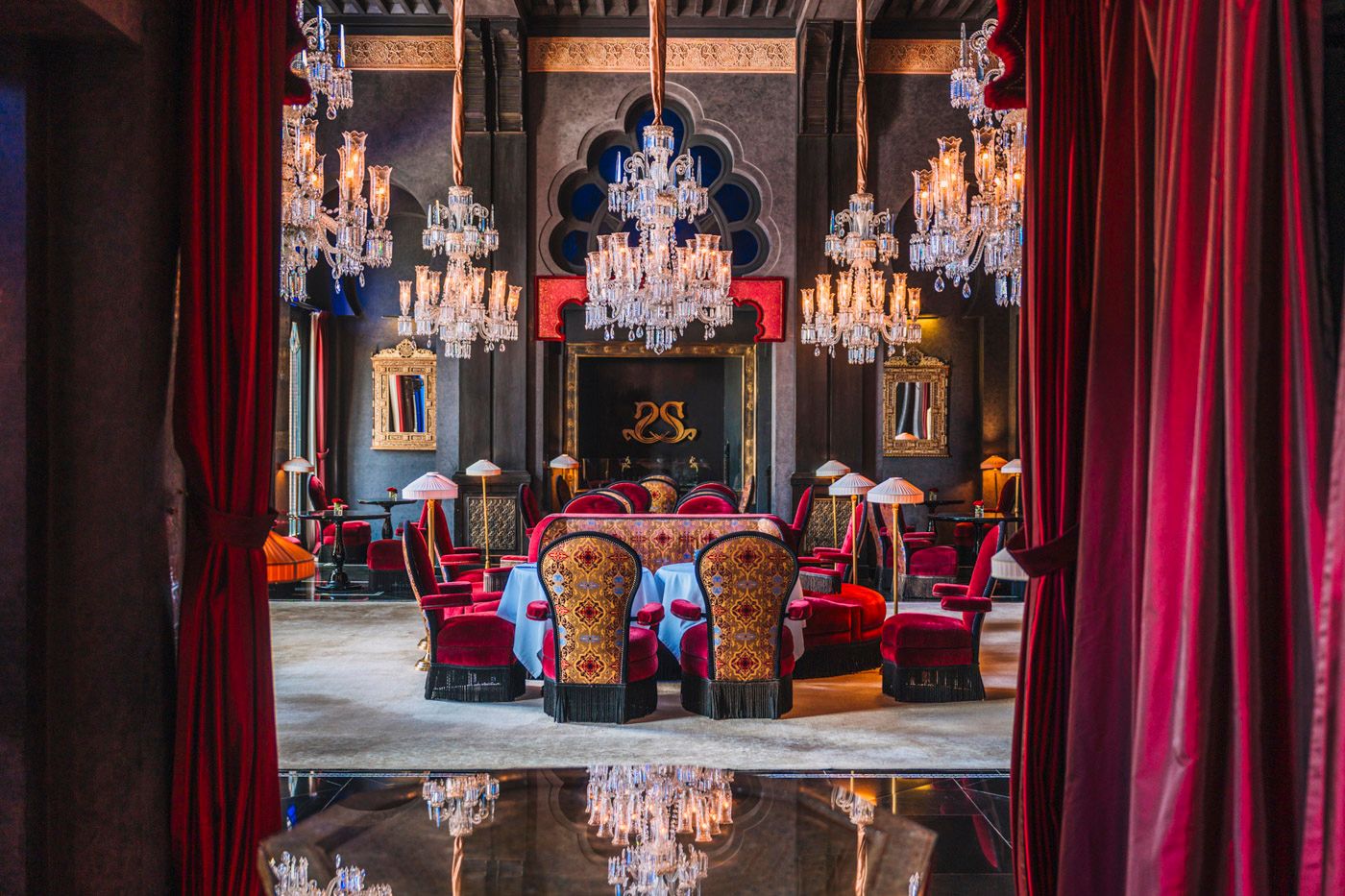 Luxurious dining room with crystal chandeliers, red velvet curtains and ornate furniture in an opulent gothic setting.