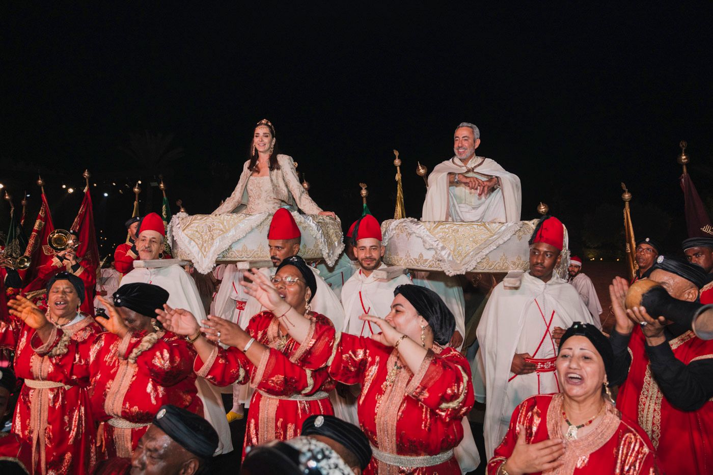 A group of performers in red robes gather during a night ceremony with candles and ceremonial attire.