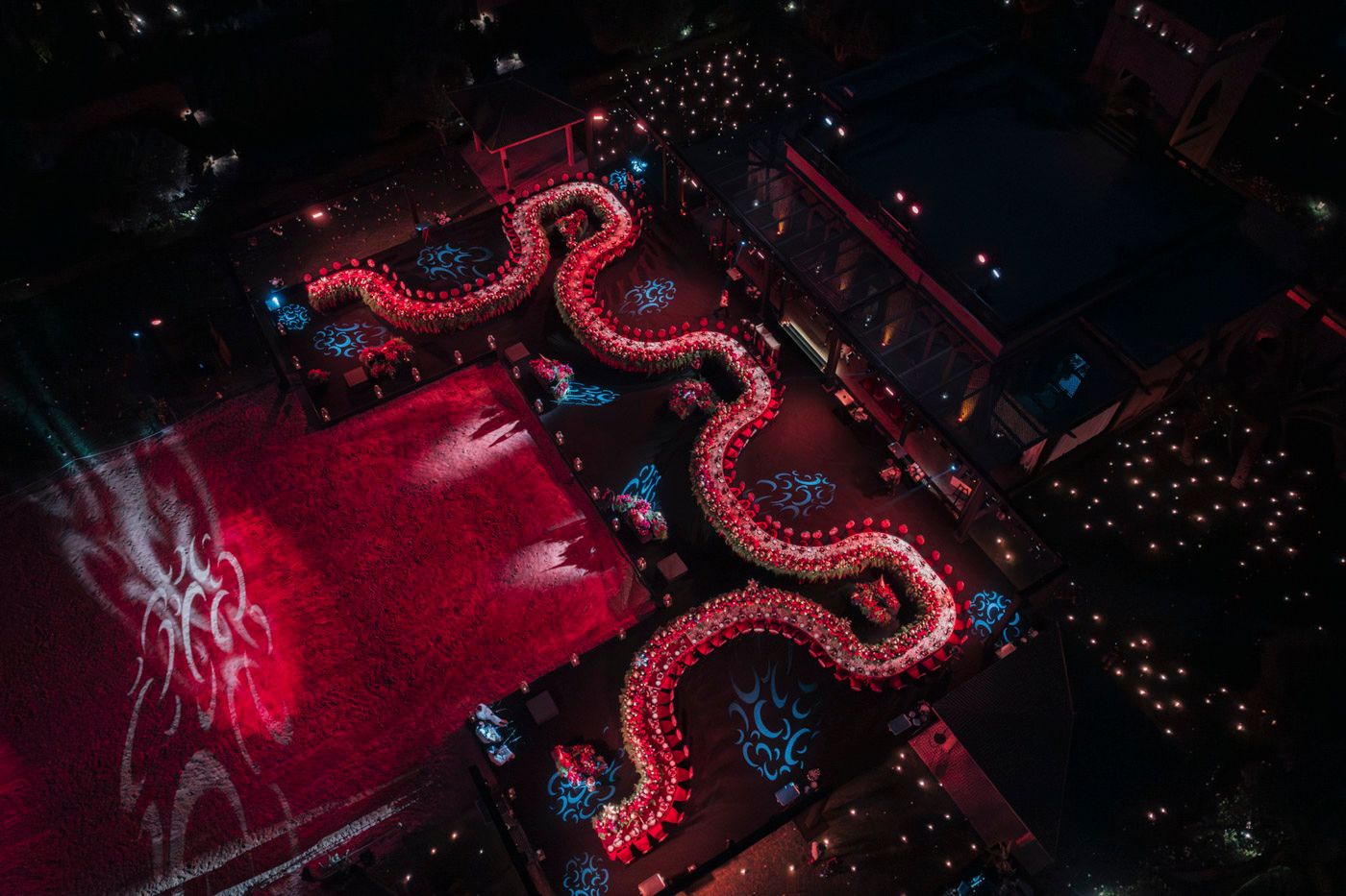 Aerial view of a winding red LED light installation creating a serpentine pattern on dark ground at a nighttime event.