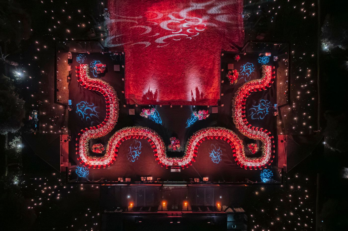 Red neon stage design with geometric patterns glows dramatically against a dark starry background during a concert performance.