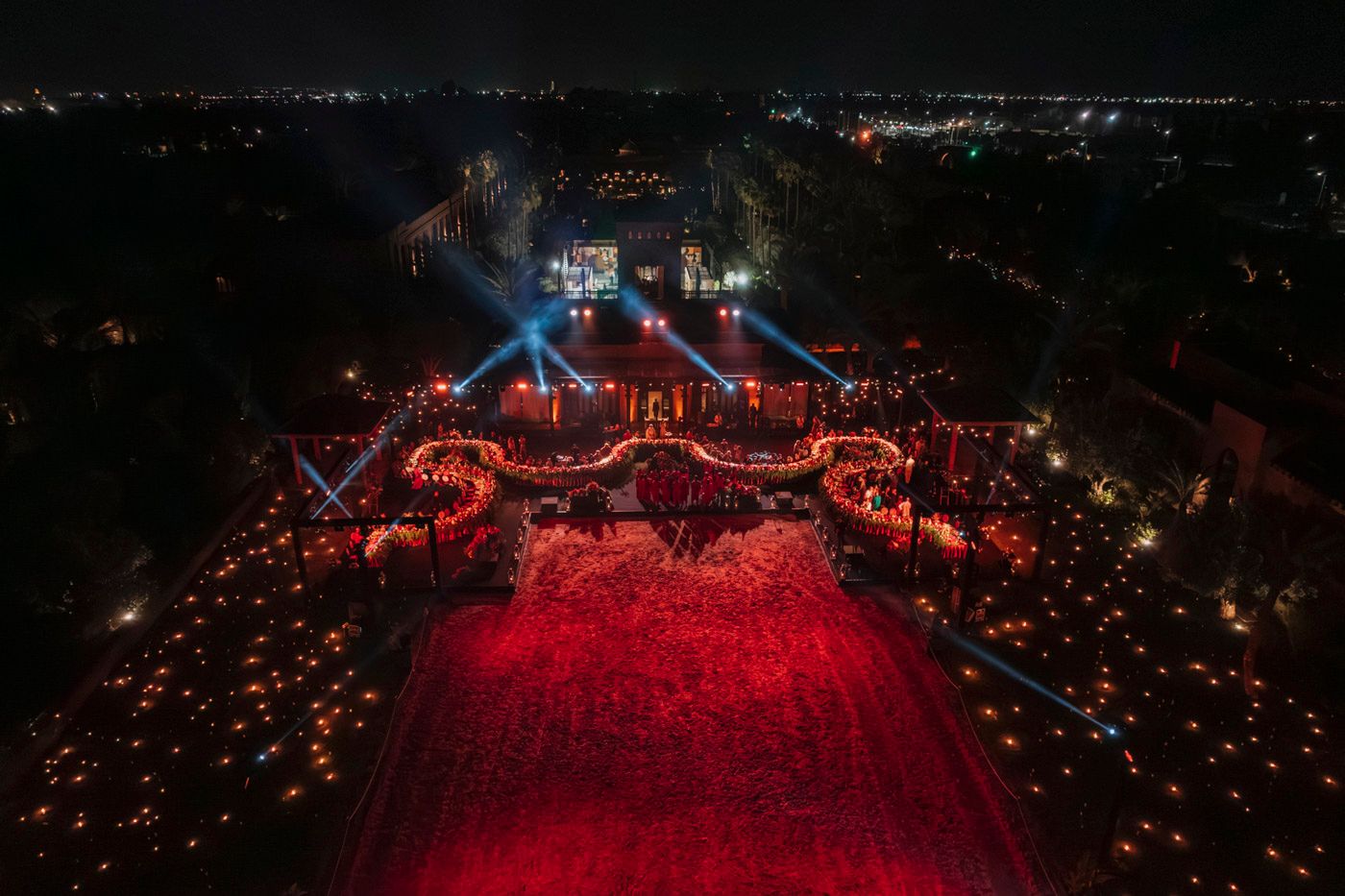 Aerial view of an outdoor concert venue illuminated in dramatic red and blue lighting with a large crowd at night.