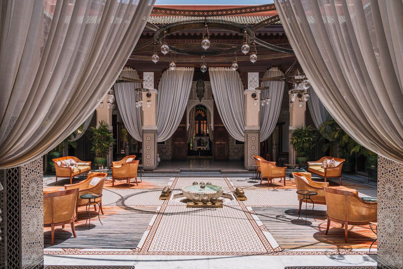 Elegant outdoor patio with draped curtains, tan leather chairs and Moroccan-style architectural details around a mosaic floor.