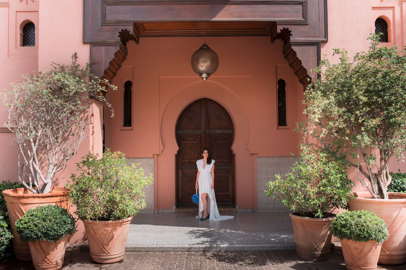 A traditional arched doorway with pink walls and potted plants at the entrance of a Mediterranean style building.