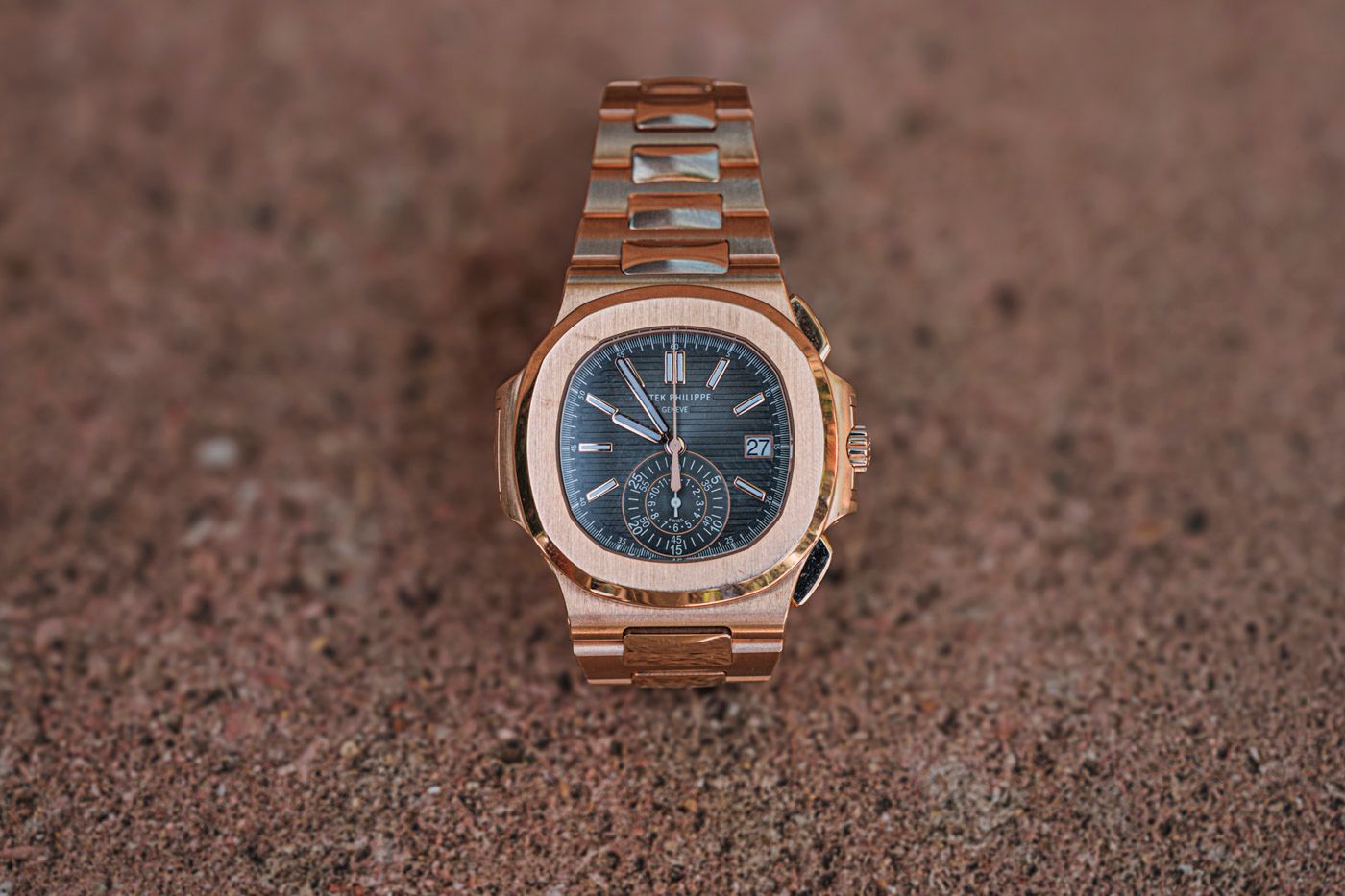Rose gold Patek Philippe Nautilus luxury watch with blue dial positioned on textured brown surface.