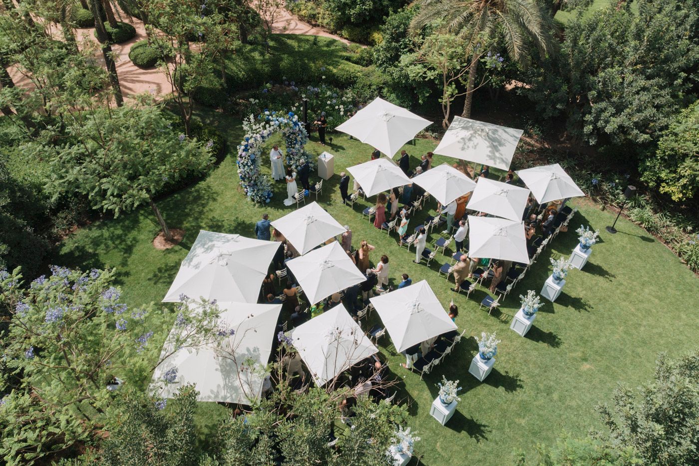 Aerial view of small white canopy tents set up for an outdoor event in a lush green garden setting.