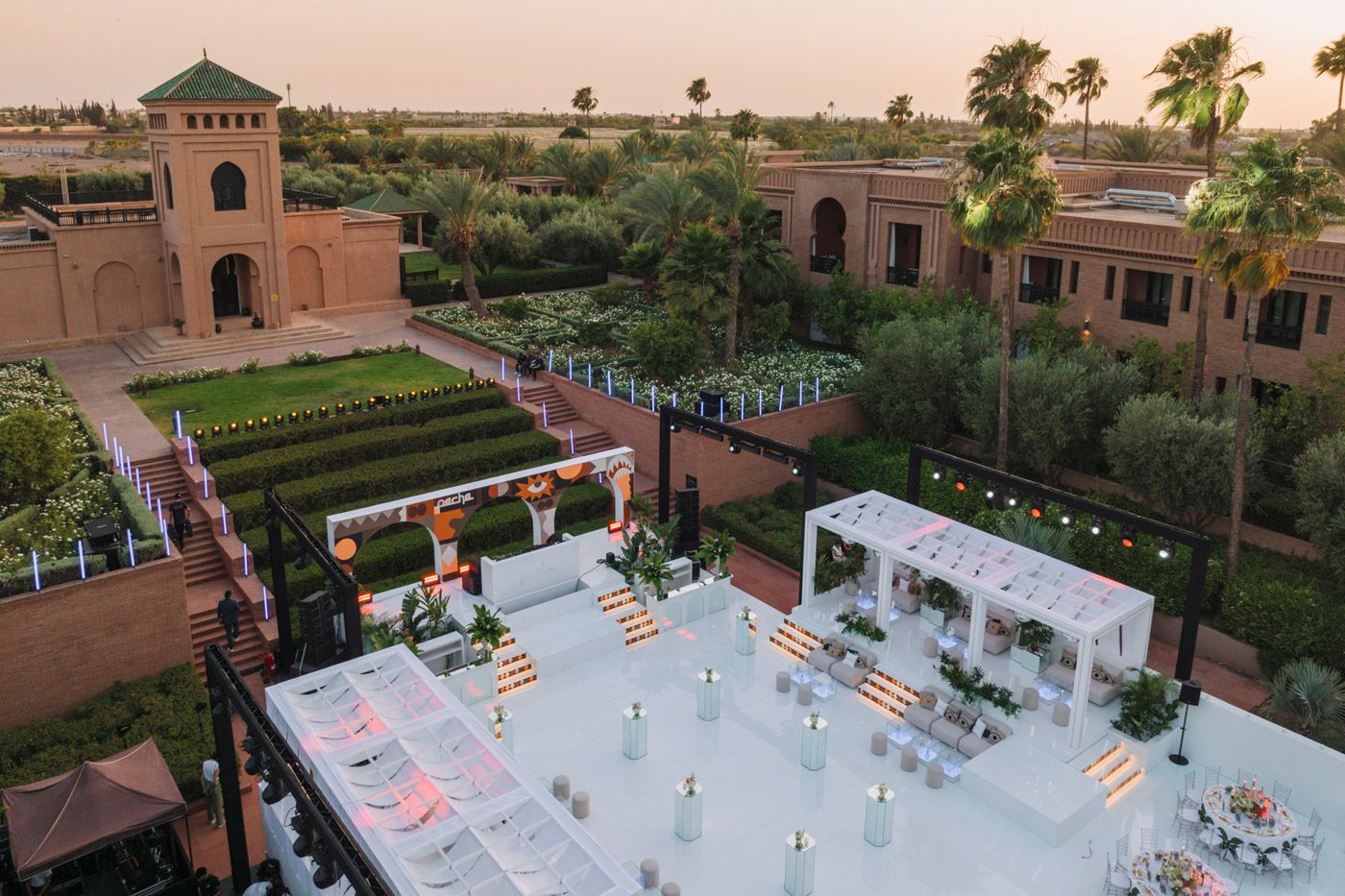 Aerial view of a luxurious outdoor event space with string lights and white seating at a Moroccan resort during sunset.