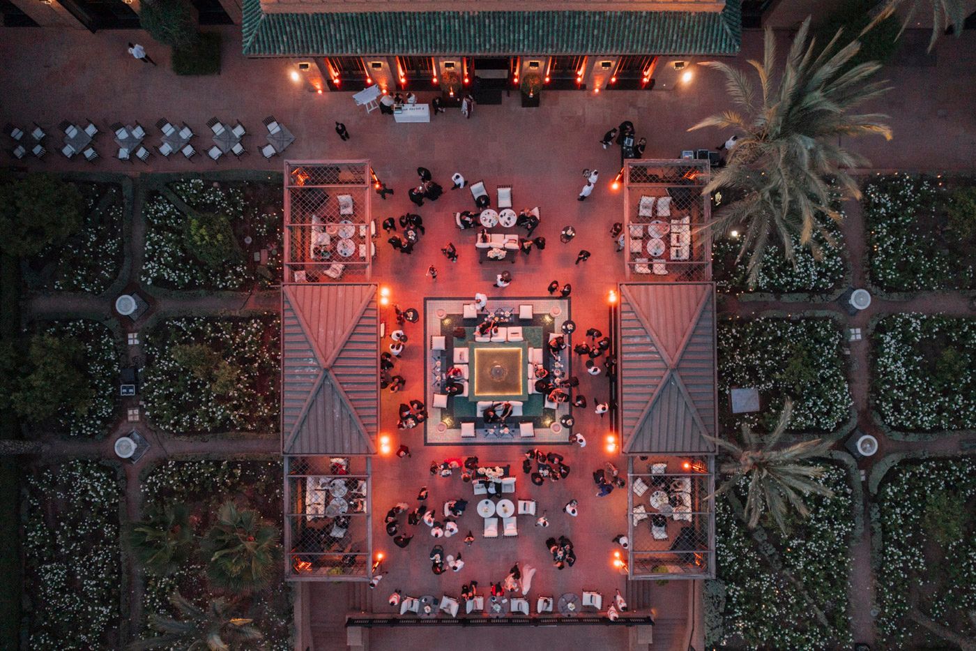 Aerial view of an outdoor restaurant courtyard with red lighting and palm trees illuminated at night.