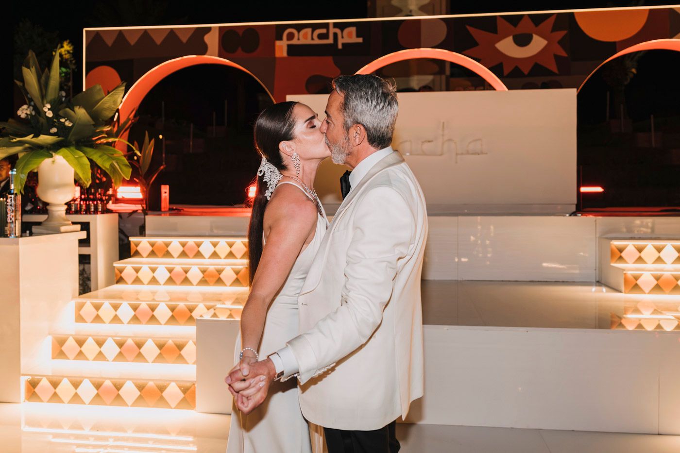 A romantic moment during the celebration with a white geometric stage backdrop illuminated by warm lighting.
