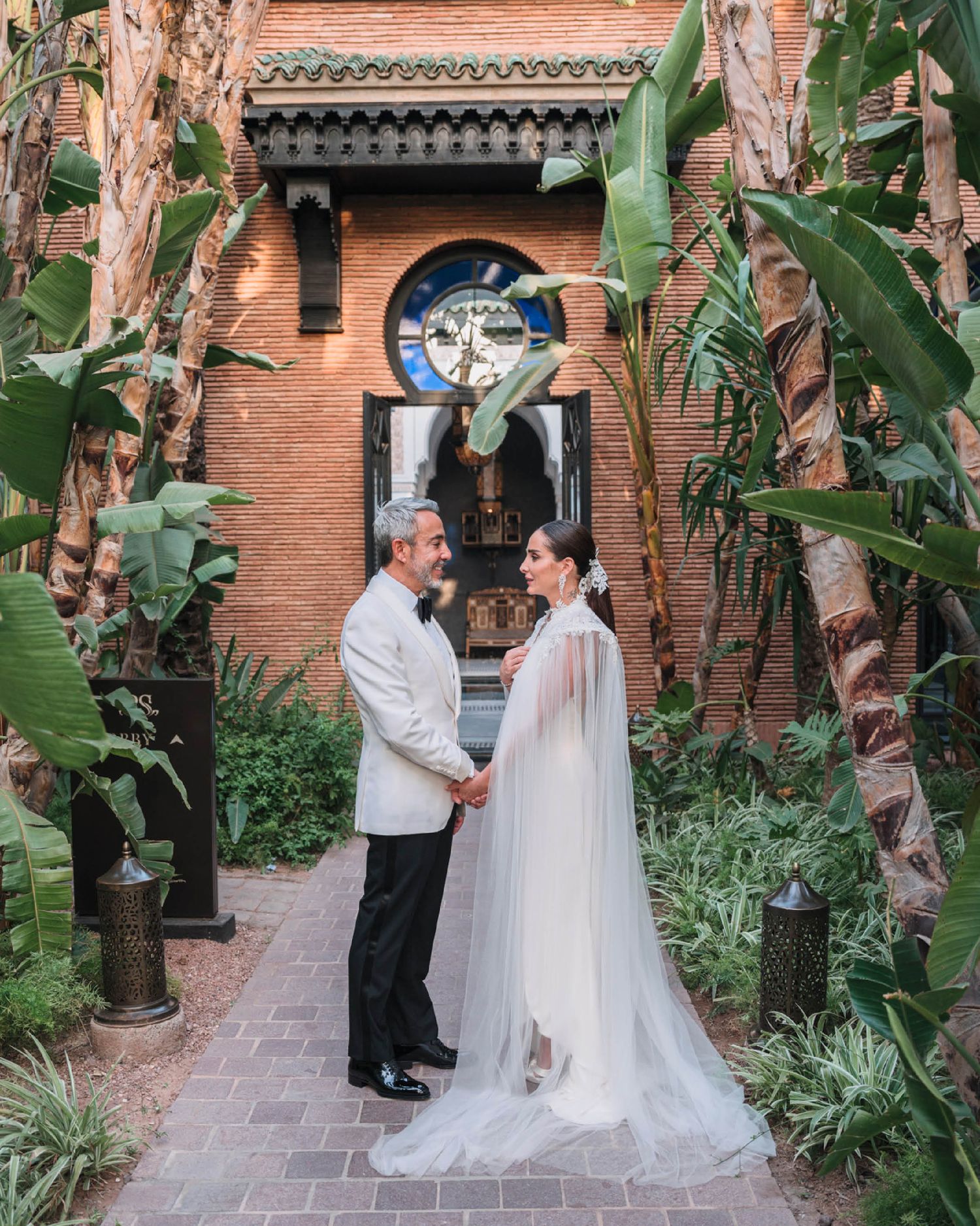 A romantic wedding moment captured in a lush garden courtyard with terracotta walls and tropical plants.