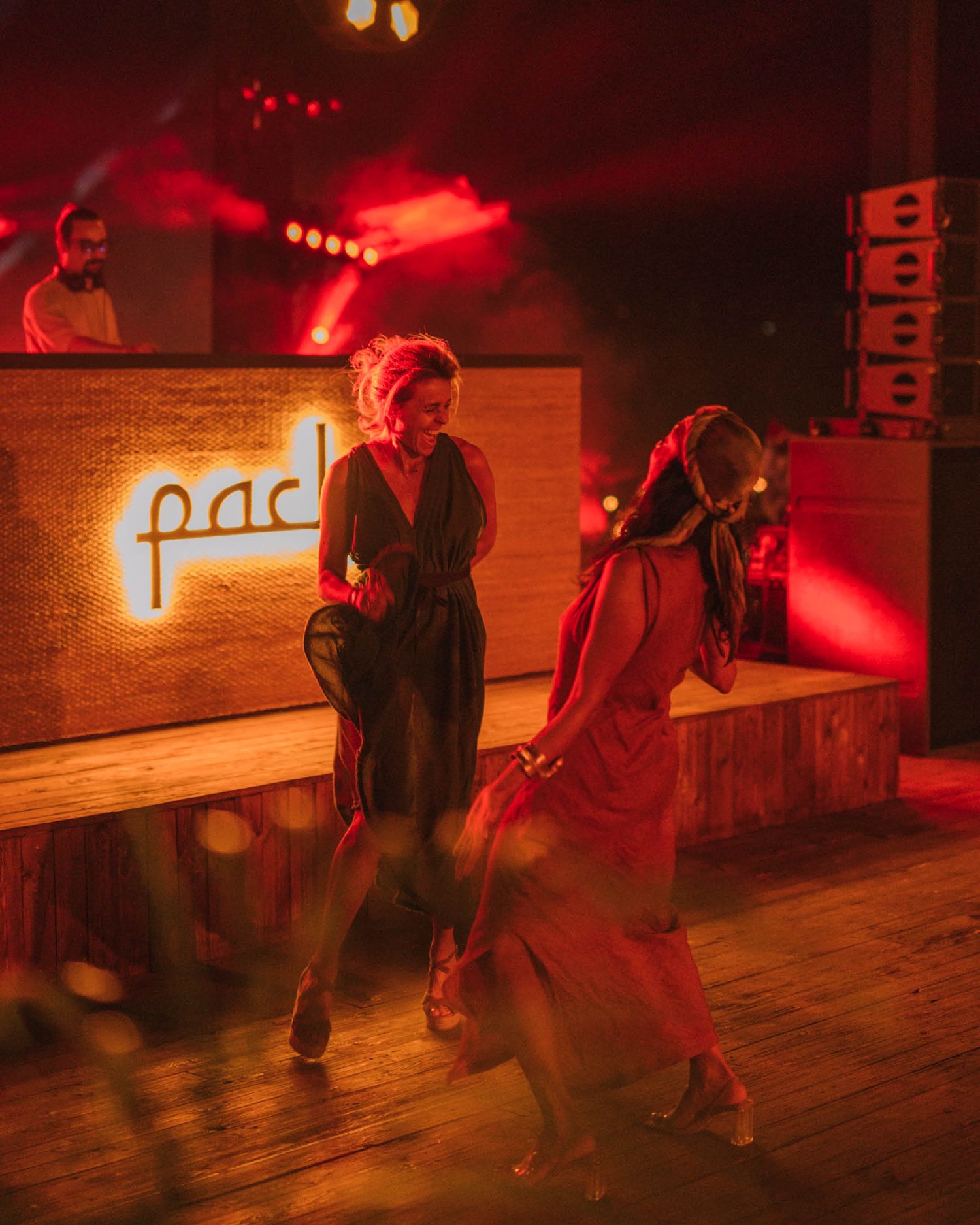 Two figures dance energetically in a dark nightclub with red lighting and a neon sign.