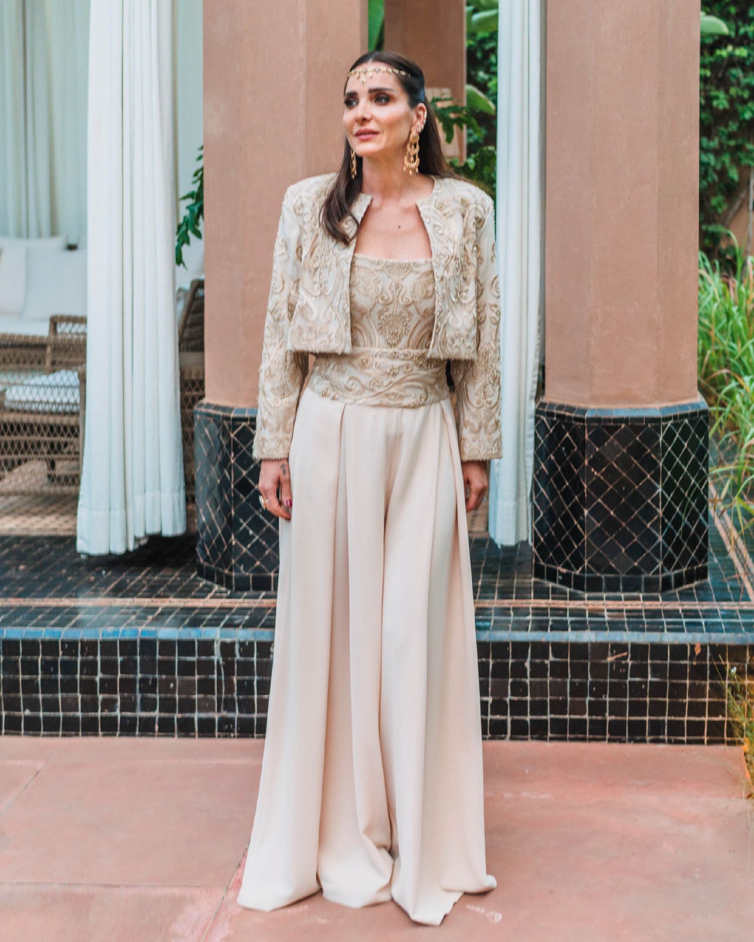 Elegant woman wearing a champagne-colored evening ensemble with lace jacket and flowing palazzo pants at an outdoor venue.