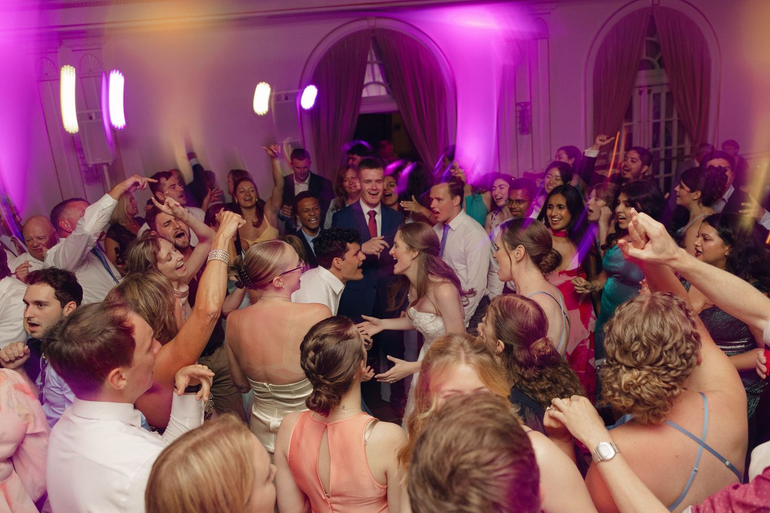 Wedding reception dance floor filled with guests dancing and celebrating under vibrant purple lighting.