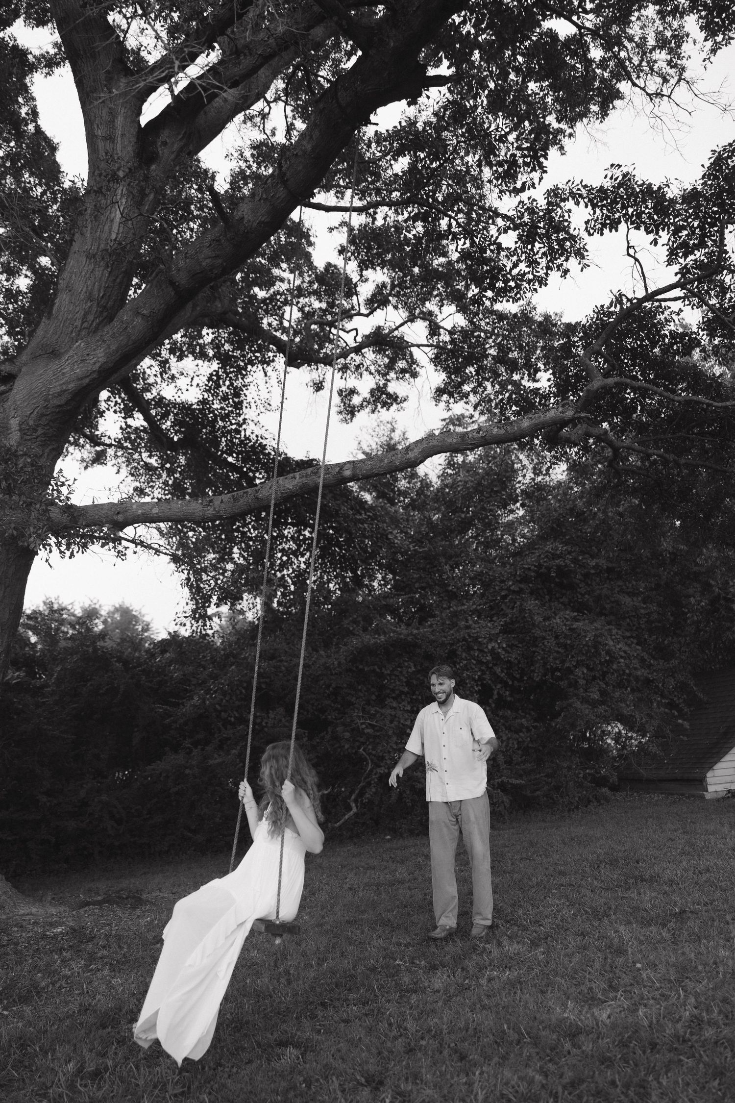 A series of black and white photos showing a figure swinging on a rope swing beneath a large tree in a grassy field.